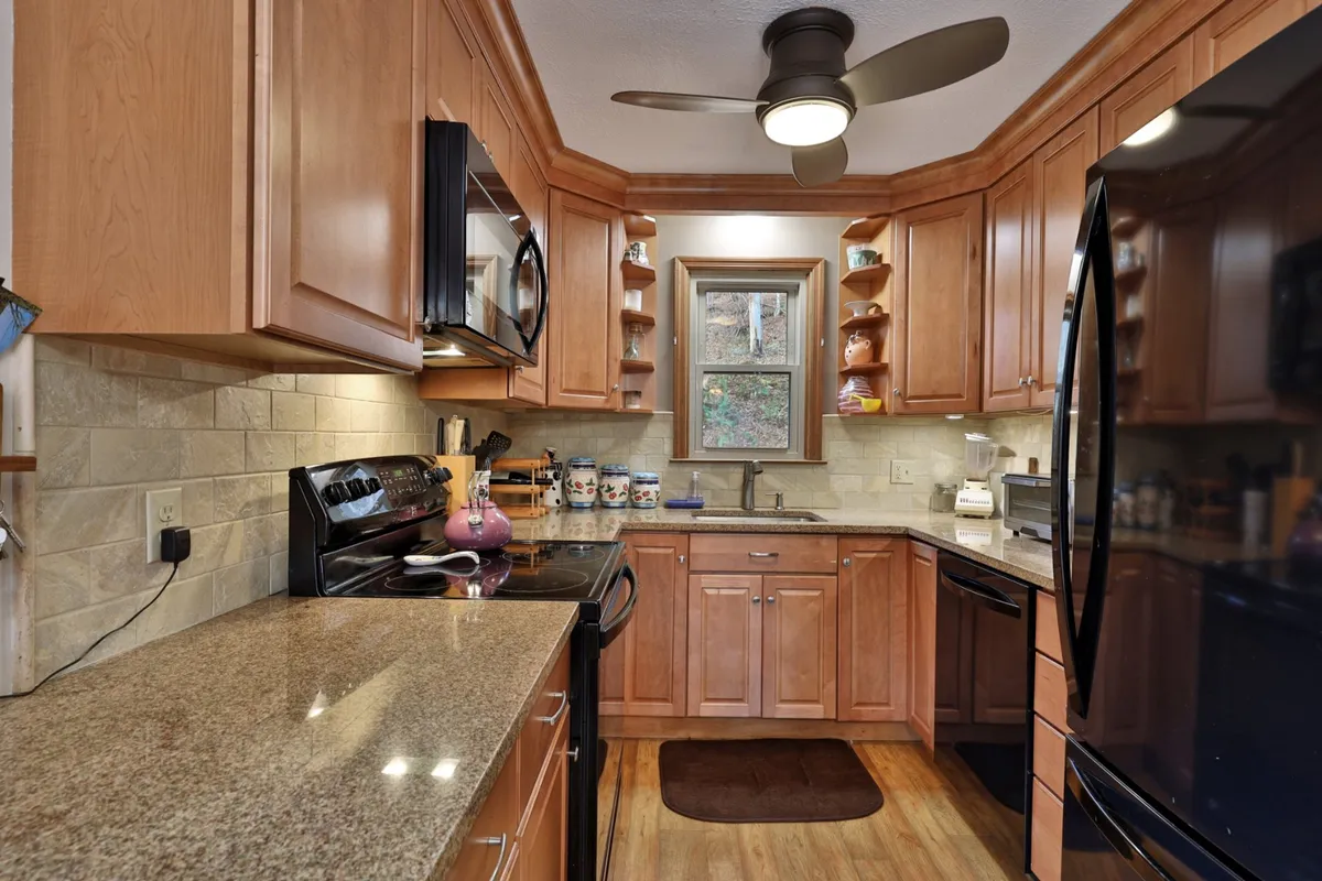 A warm kitchen scene with granite countertops, stainless steel appliances, wooden cabinets, and a window overlooking a tranquil outdoor view. The layout suggests a space for family gatherings and relaxed meal prep, with plenty of room for multiple cooks.