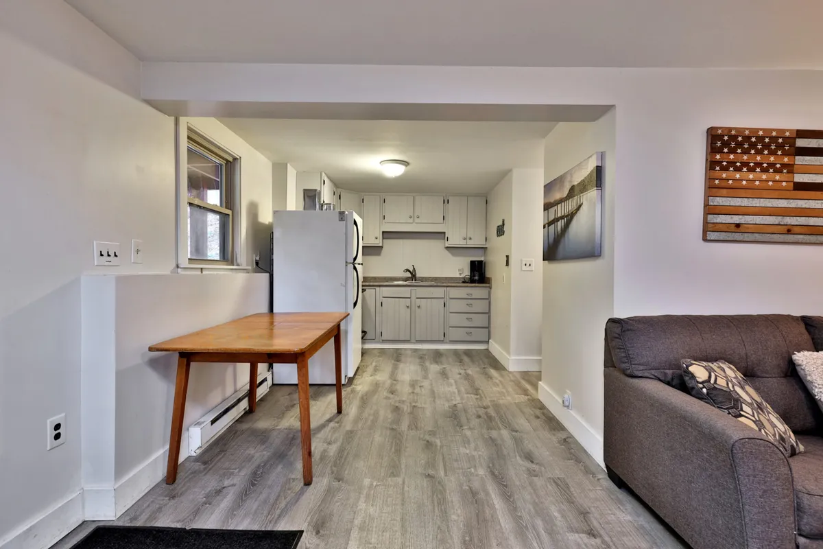 A bright, comfortable open-plan interior featuring a dining table, kitchen area, and a cozy sofa—all in one inviting space. The setup invites families and friend groups to gather, cook, and share meals after a day spent outside.