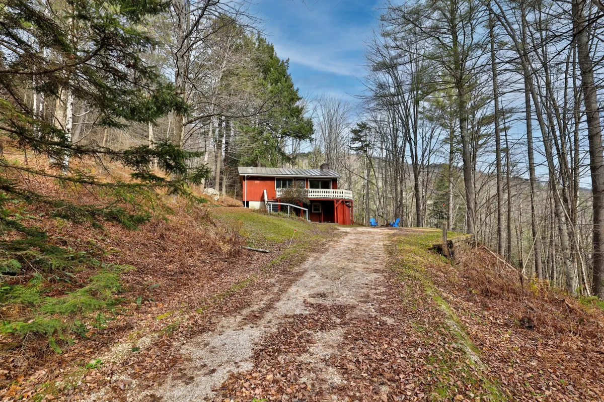 The red house stands prominently with a gravel path leading to it, surrounded by serene trees. The deck area hints at opportunities for outdoor gatherings and storytelling under the stars, evoking a sense of anticipation for winter fun and cozy evenings.