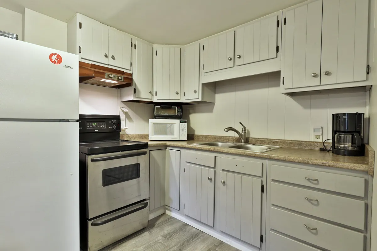 A bright, homey kitchen featuring a refrigerator, oven, sink, microwave, and coffee maker. Ample counter space and cabinetry suggest a fully stocked environment ideal for meal prep and group cooking. The scene feels welcoming and ready for shared culinary moments.