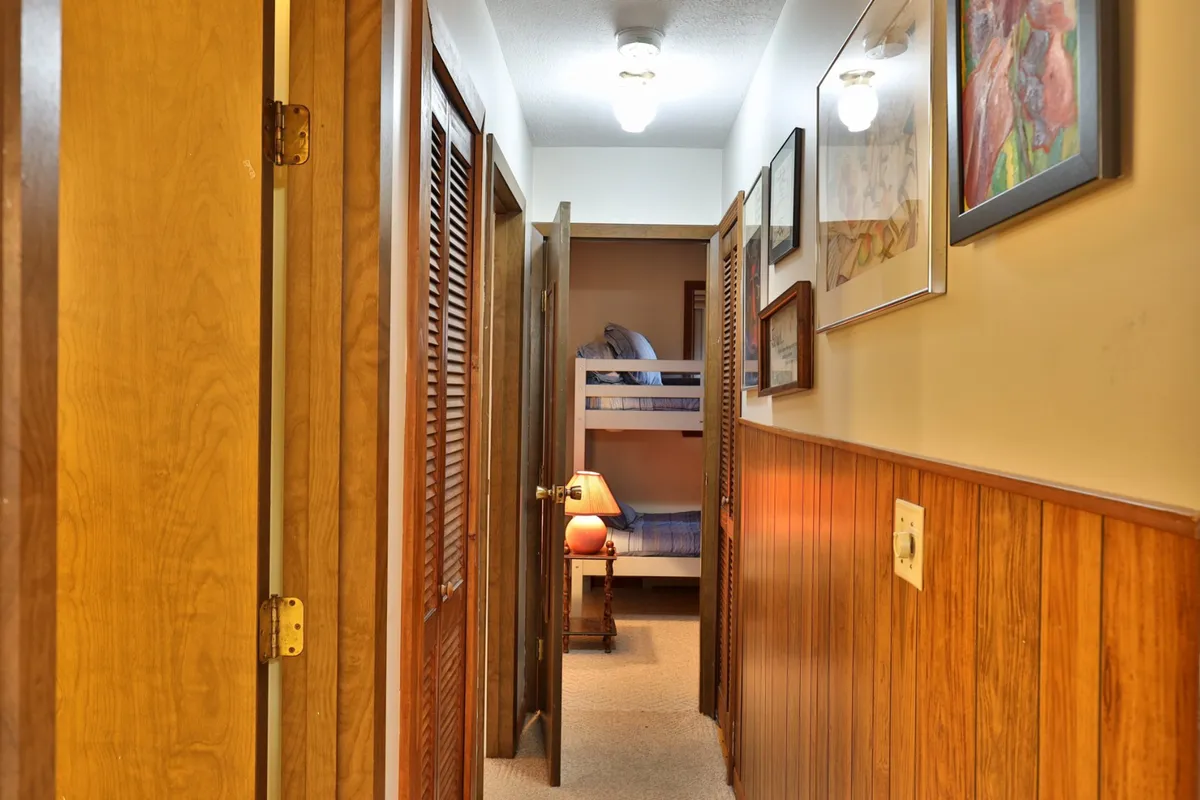 This image features a cozy bunk room with sturdy wooden bunk beds, decorative wall art, and a table lamp, providing a playful yet comfortable environment. The space invites family gatherings, quiet reading, and restful sleep, and the presence of a ladder is subtly visible, underscoring the need for supervision with children.